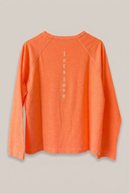 SENCES THE LABEL Glow Hour Langarmshirt in Orange, Rückseite vor Greige-Hintergrund