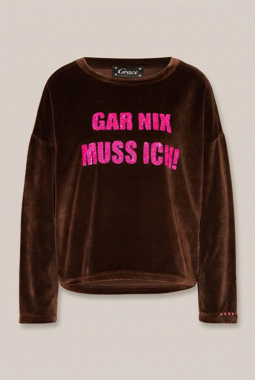 GRACE Langarmshirt in Moccabraun mit intensiv pinkem Pailletten-Schriftzug vor Greige-Hintergrund