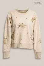 Handbesticktes TheShirtProjekt Sweatshirt in hellem Beige-Melange mit floraler Perlenstickerei vor warmem Greige-Hintergrund